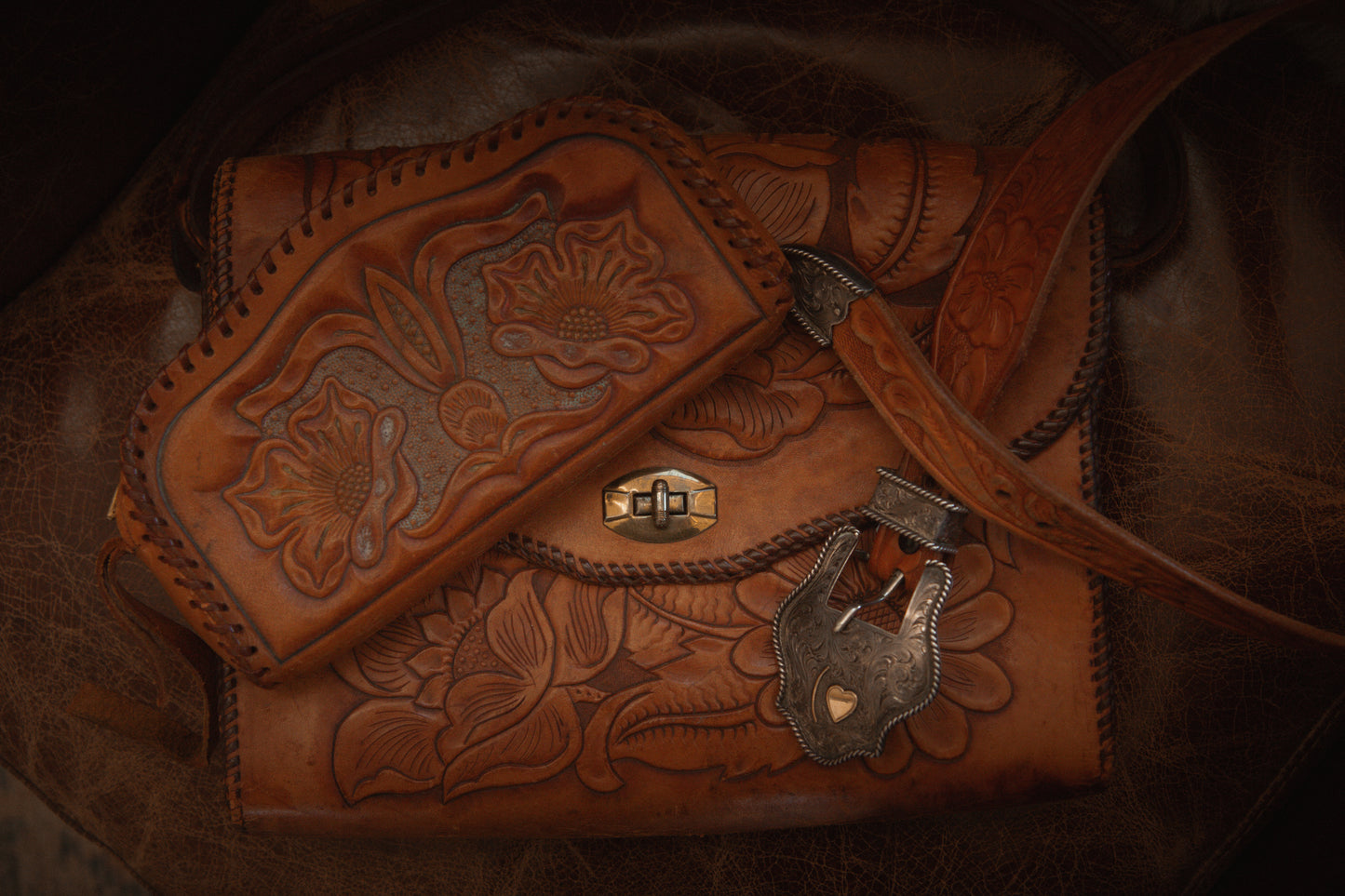 Brown leather bag with intricate designs and a padlock on a dark background