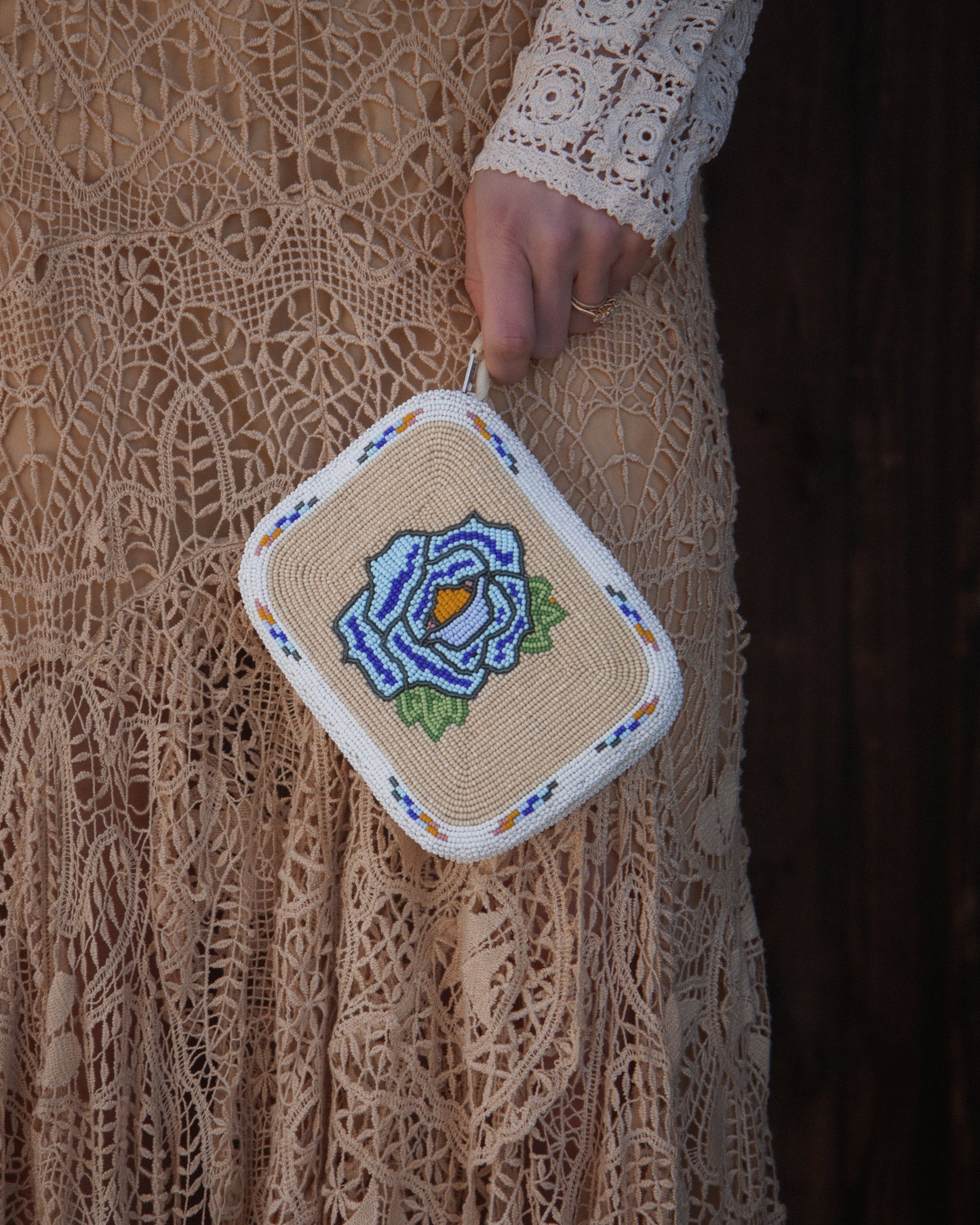 Handmade beaded purse with floral design held by a person wearing a lace dress.