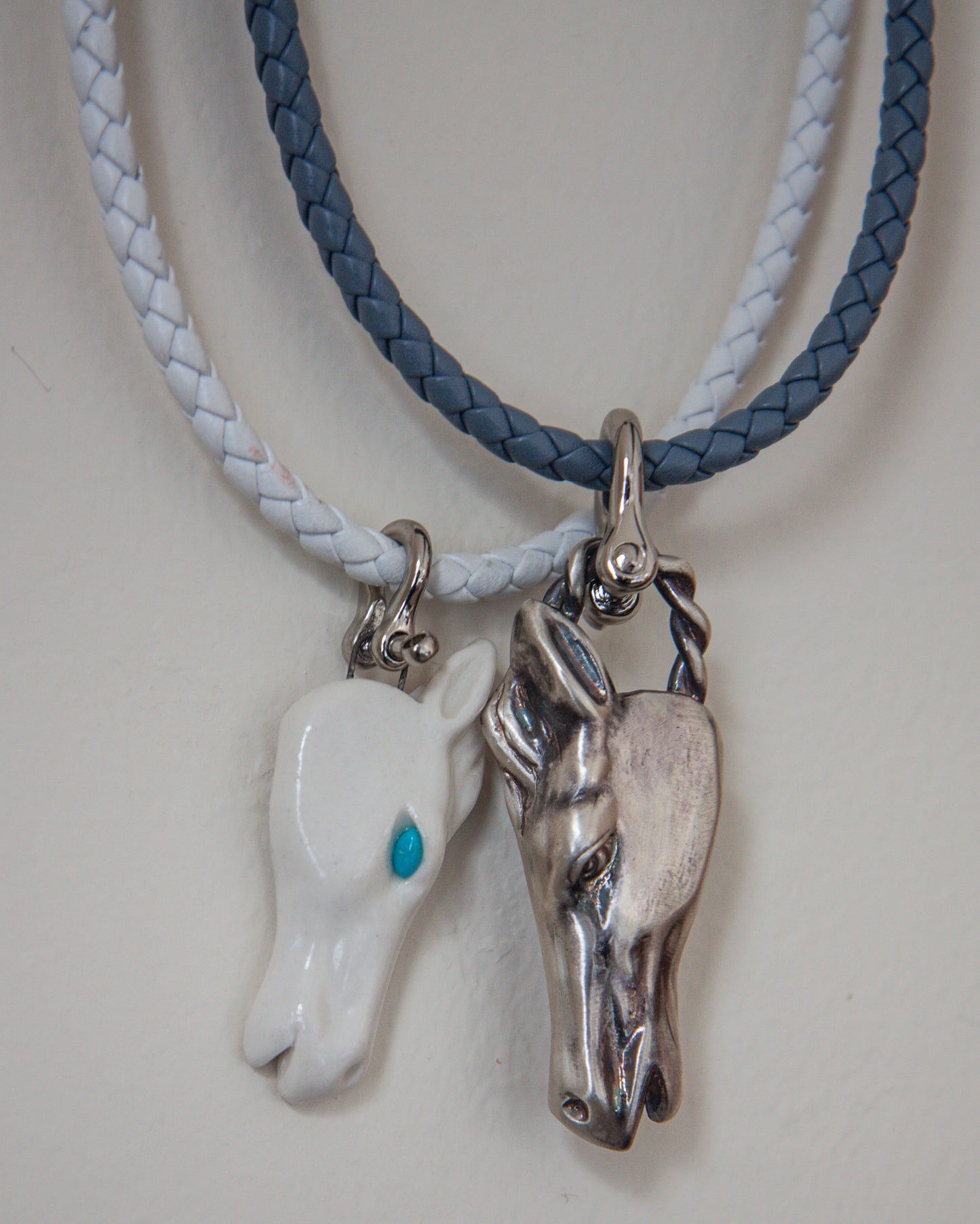 Two horse head pendants on braided leather cords against a white background