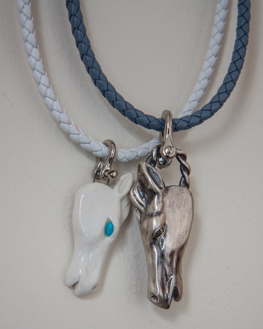 Two horse head pendants on braided leather cords against a white background