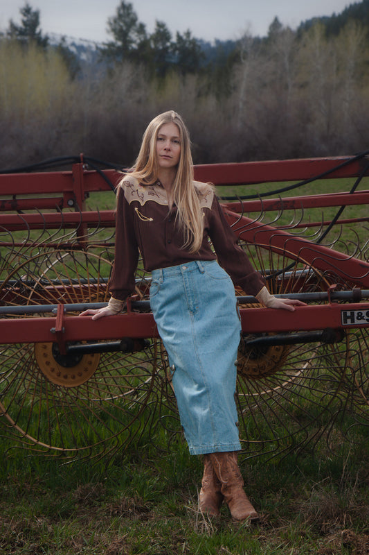 Woman standing next to a red farm implement in a field with trees in the background