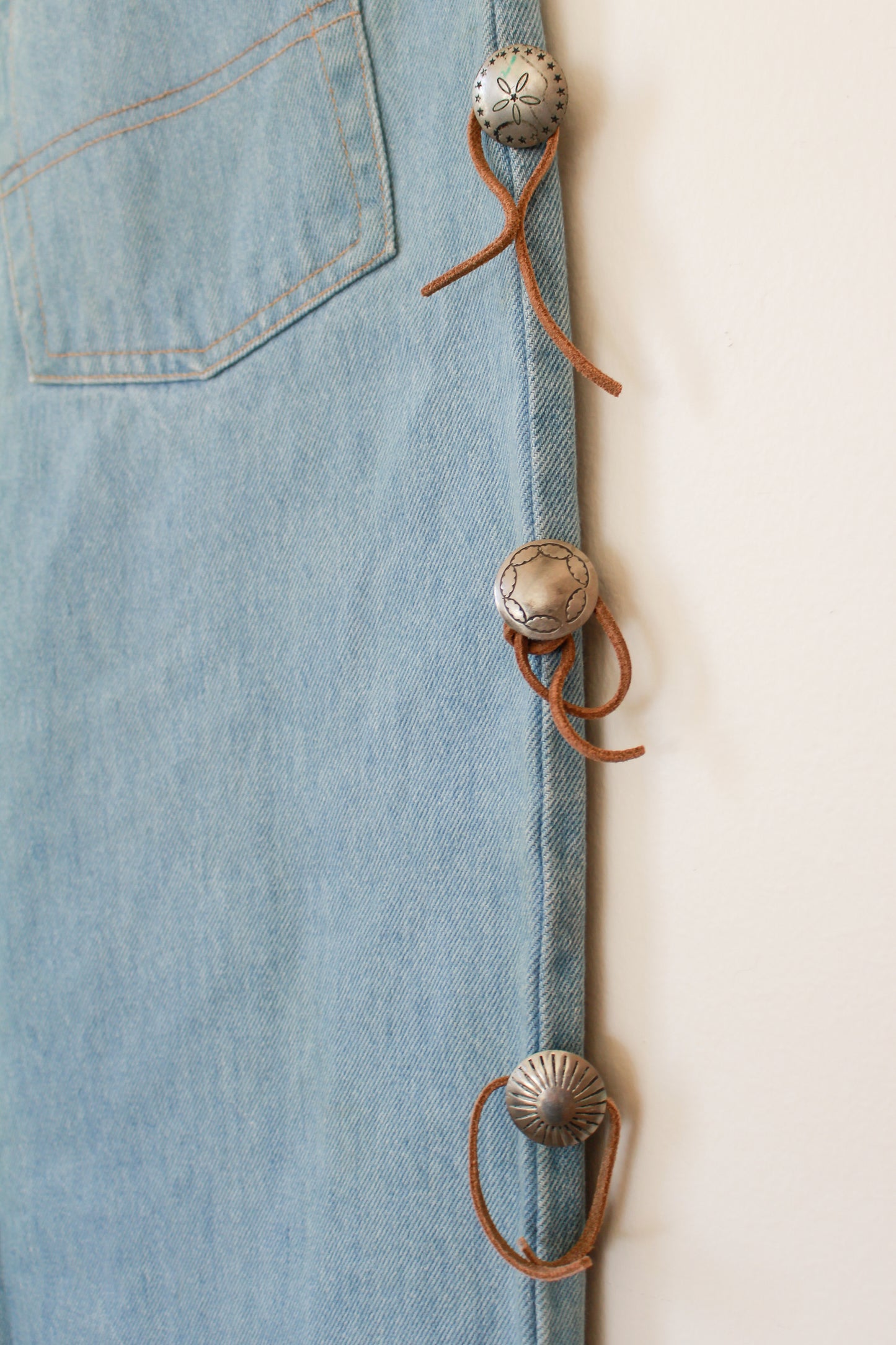 Close-up of a denim jacket with decorative buttons and leather strap on a light background