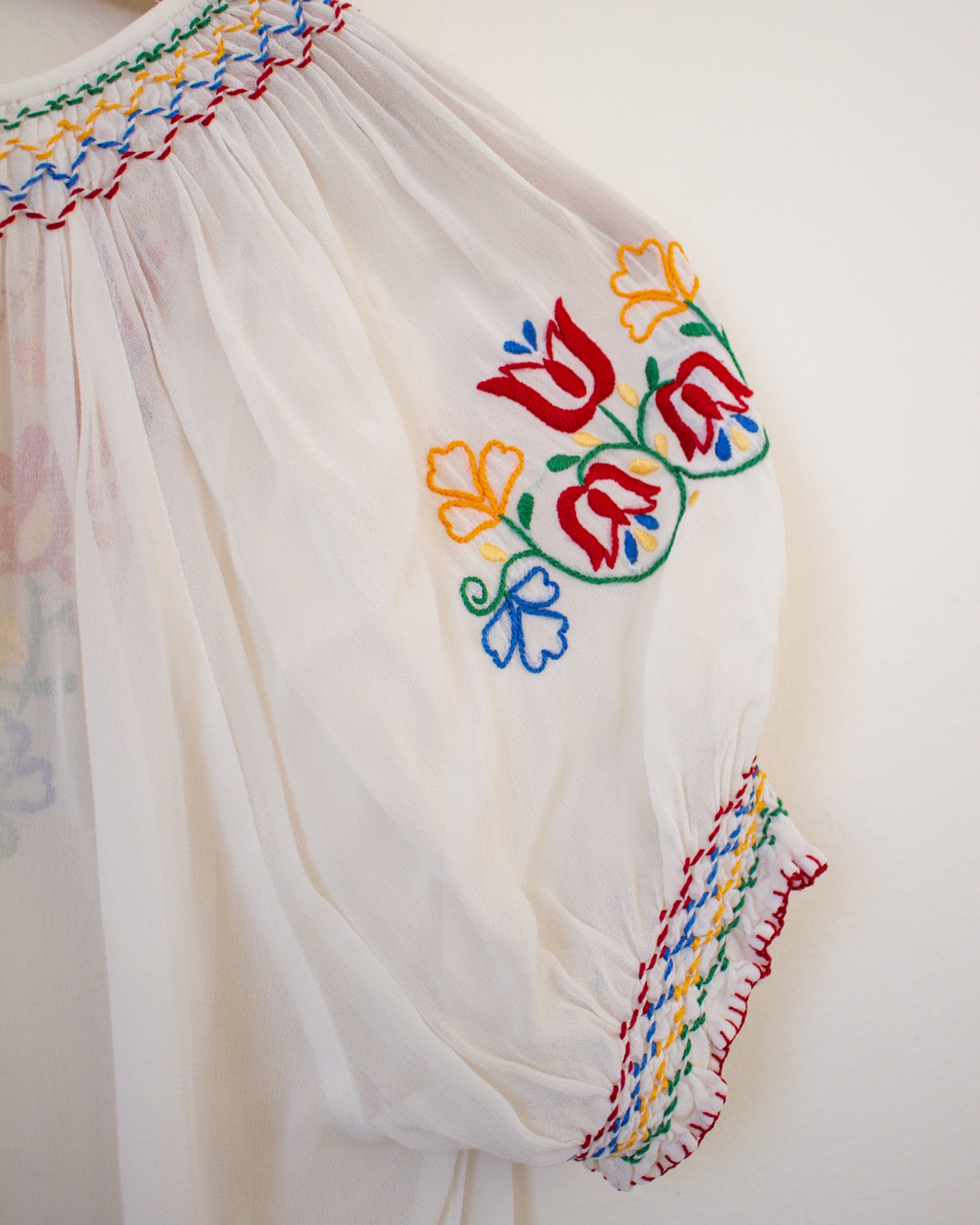 White garment with colorful floral embroidery on a plain background