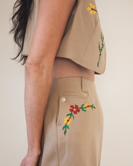 Person wearing a beige outfit with floral embroidery on a plain background