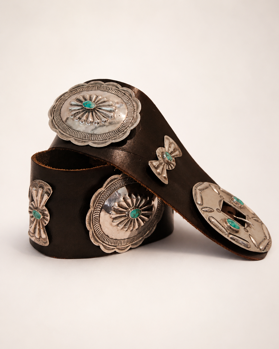 Brown leather belt with silver concho-style fastenings on a beige background