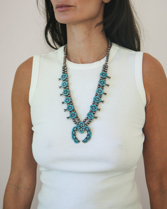 Woman wearing a long, beaded necklace with turquoise stones on a plain background