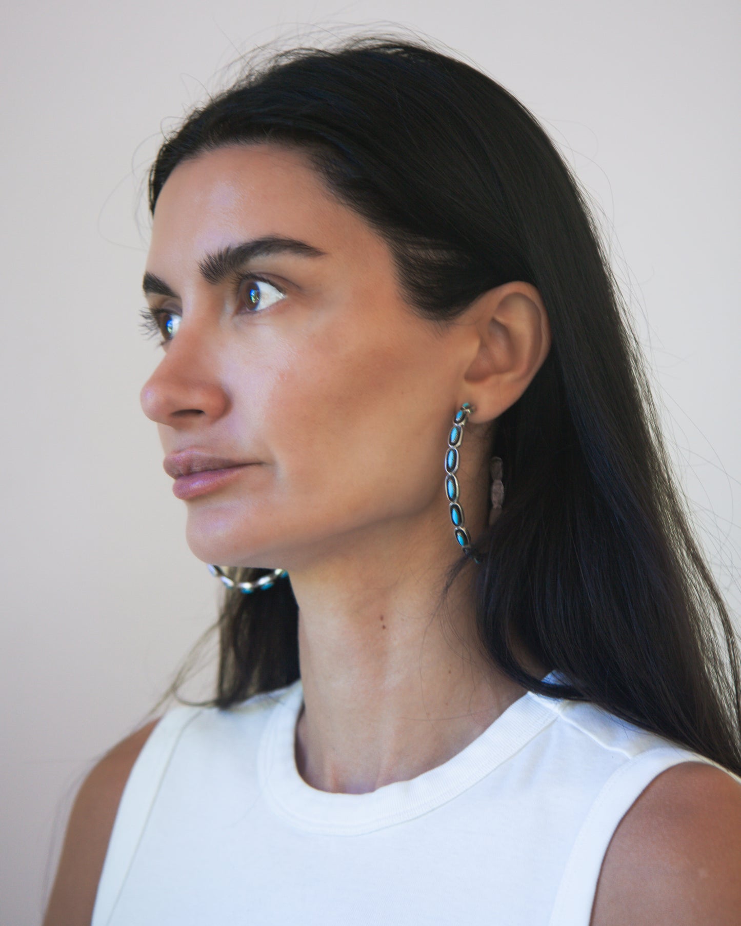Woman wearing turquoise and silver hoop earrings with a white sleeveless top with a neutral background