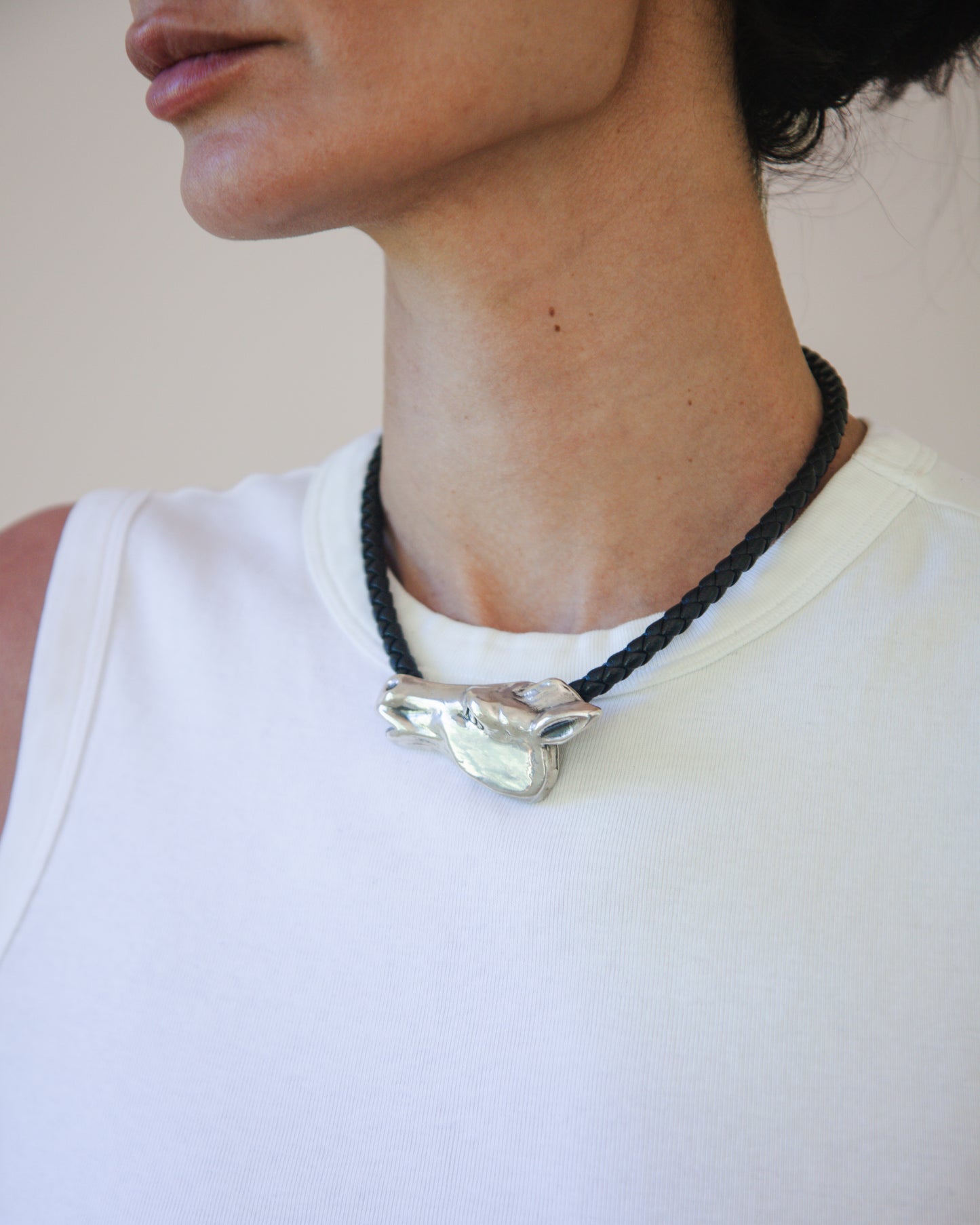 Person wearing a necklace with a silver horse pendant on a plain background