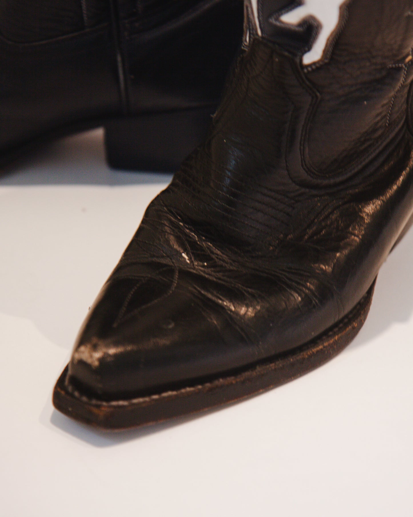 Close-up of a worn black leather cowboy boot toe on a white background