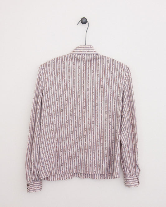 A long-sleeve button-up shirt with horse bit pattern in vertical stripes in dusty pink and brown and white, hanging on a black metal hanger against a plain white wall.