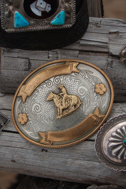 Decorative belt buckle with a horse and rider design on a wooden surface