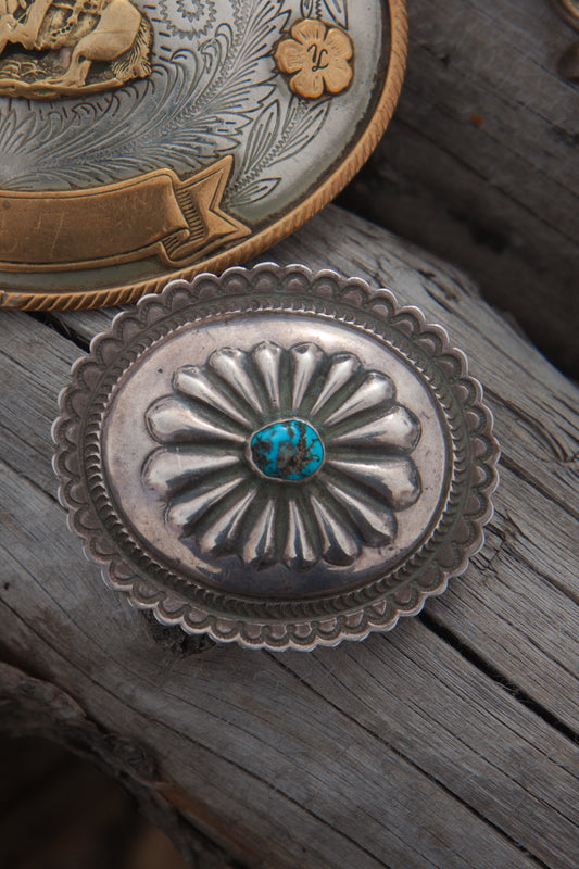 Silver concho with turquoise stone on a wooden surface