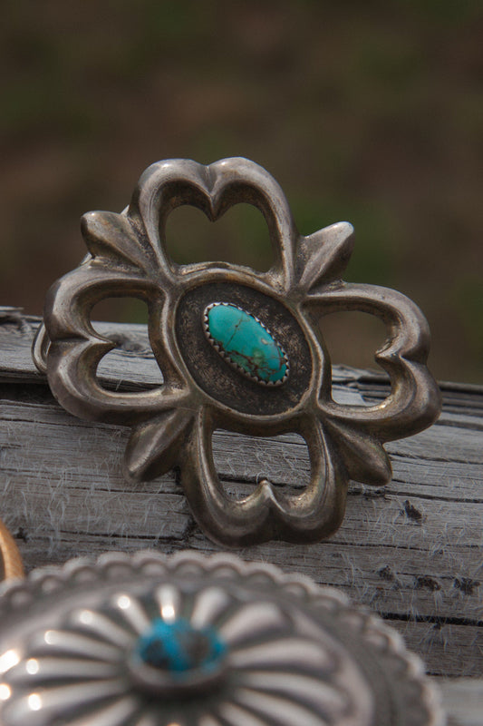 Silver concho with turquoise stone on a wooden surface