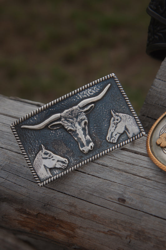 Metallic longhorn belt buckle with two horseheads in the bottom corners