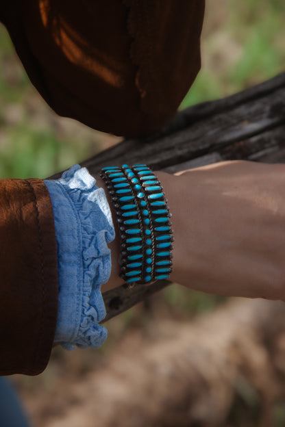 Close-up of a person's wrist wearing a blue bandage and turquoise beaded bracelet outdoors.
