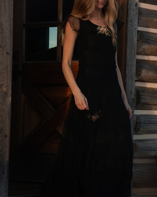 Woman wearing a black dress with floral details in a wooden interior setting