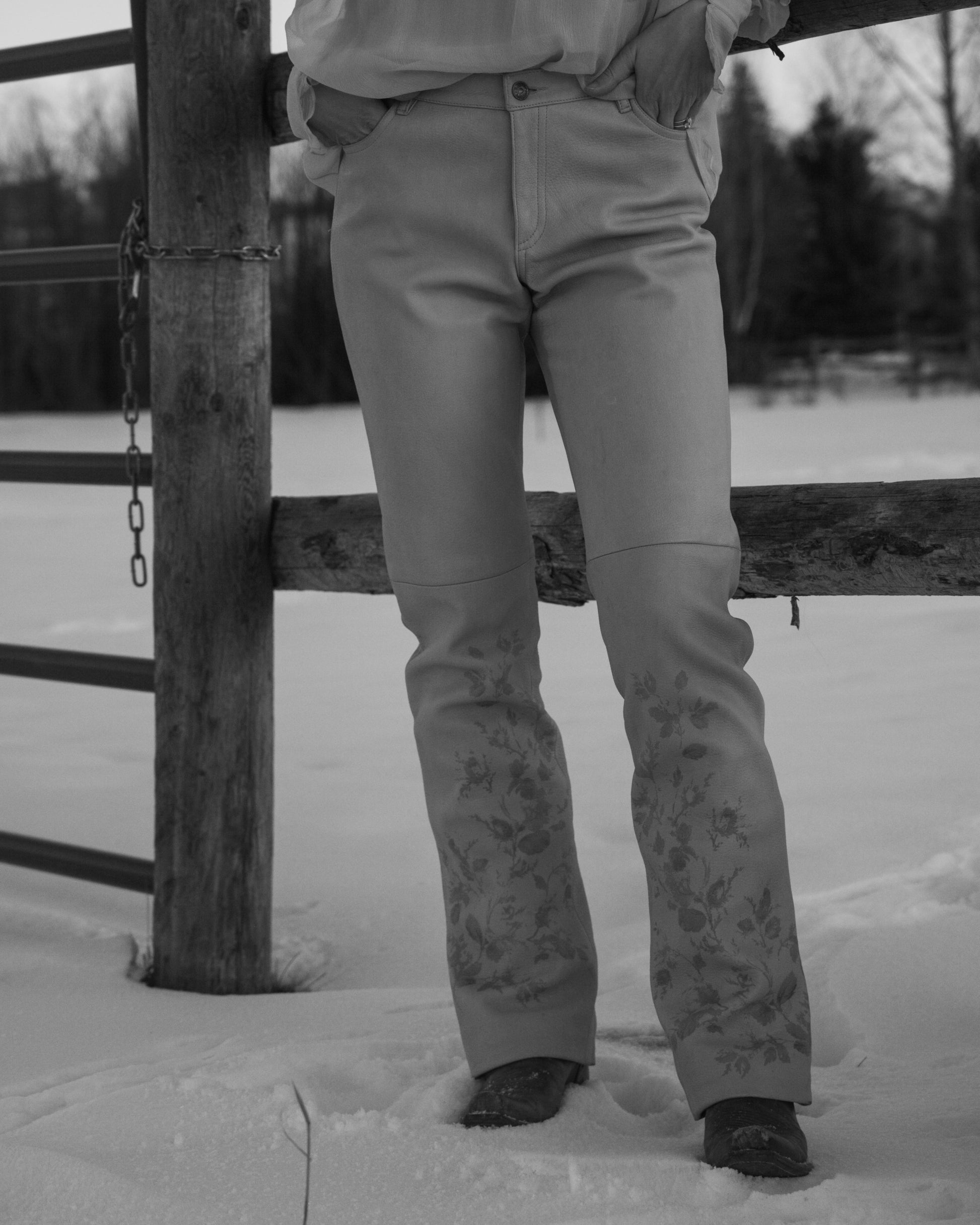 Black and white photo of a Person wearing light-colored pants with floral patterns standing in a snowy landscape.