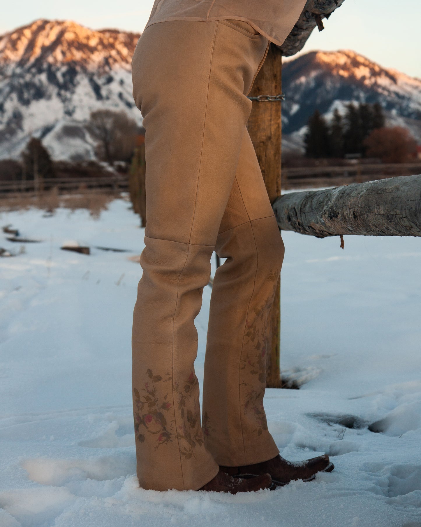 Person wearing tan pants standing in a snowy landscape with mountains in the background