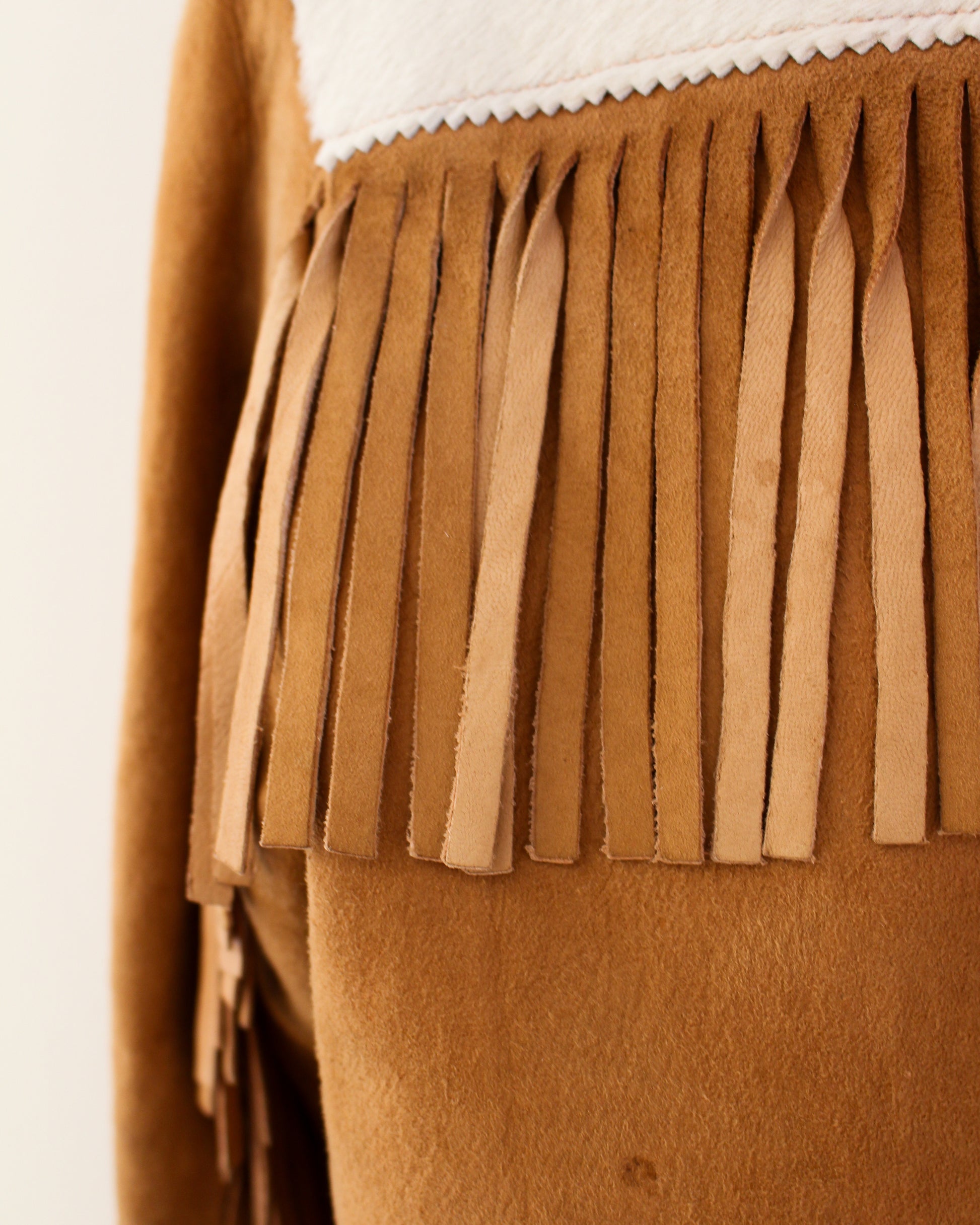 Brown suede fringe detail on a garment against a white background