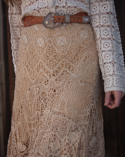 Close-up of a person wearing a lace skirt and brown belt with a decorative buckle.