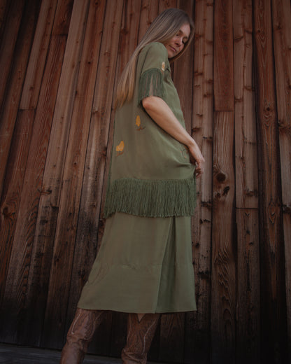 Woman wearing a green dress with fringe against a wooden wall