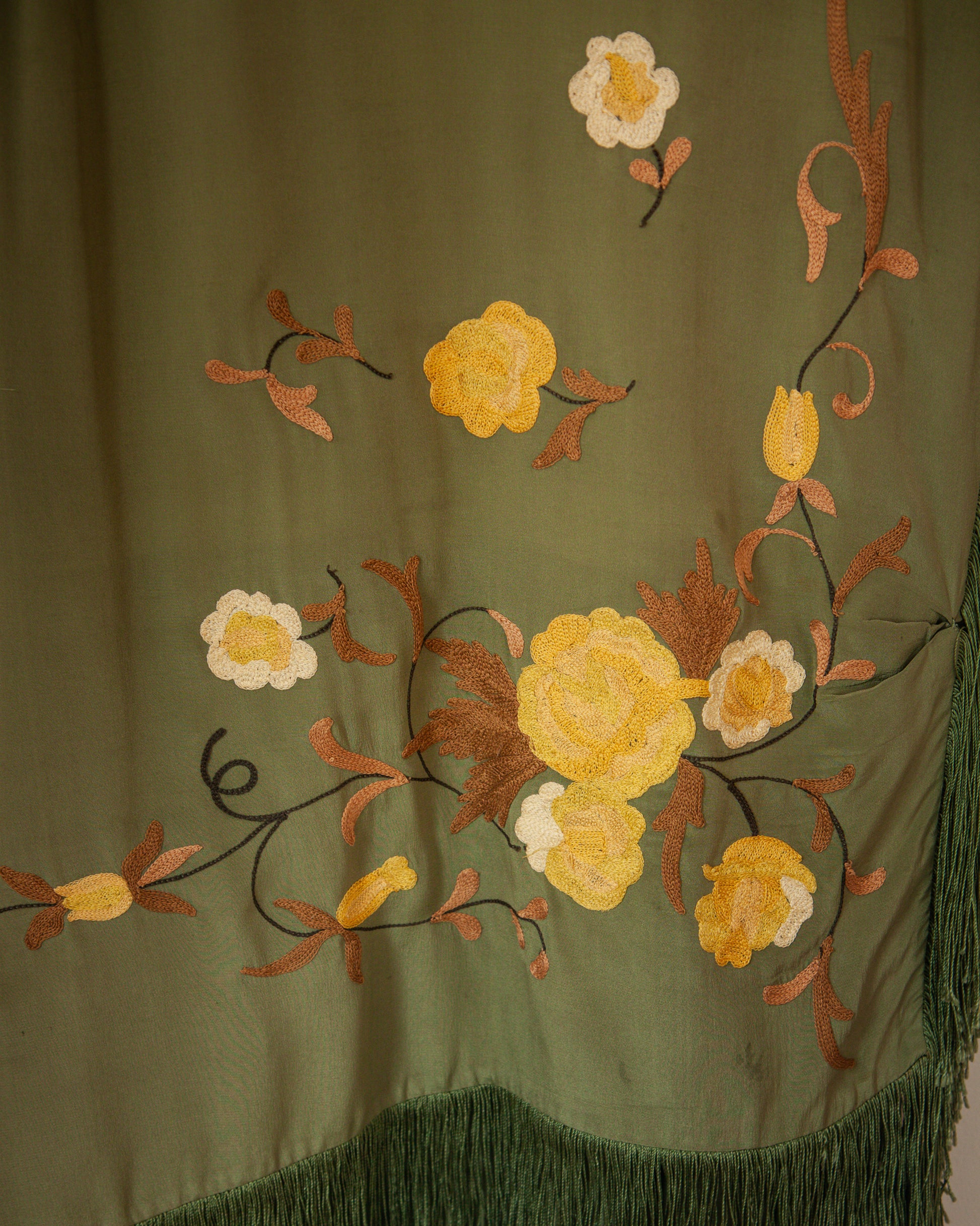 Embroidered floral design on a green fabric with yellow, white, and brown flowers.