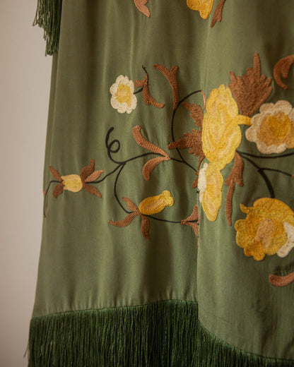 Green embroidered fabric with floral patterns and fringes on a plain background
