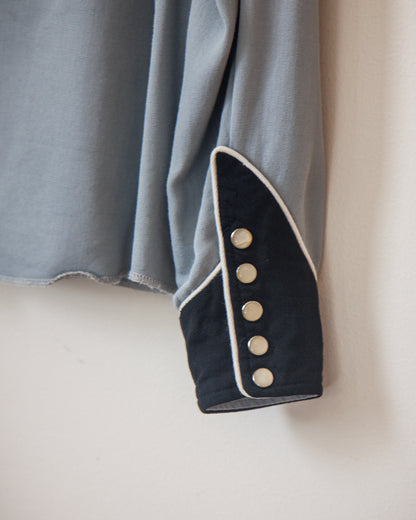 Close-up of a garment with blue fabric and black trim featuring white buttons on a neutral background.