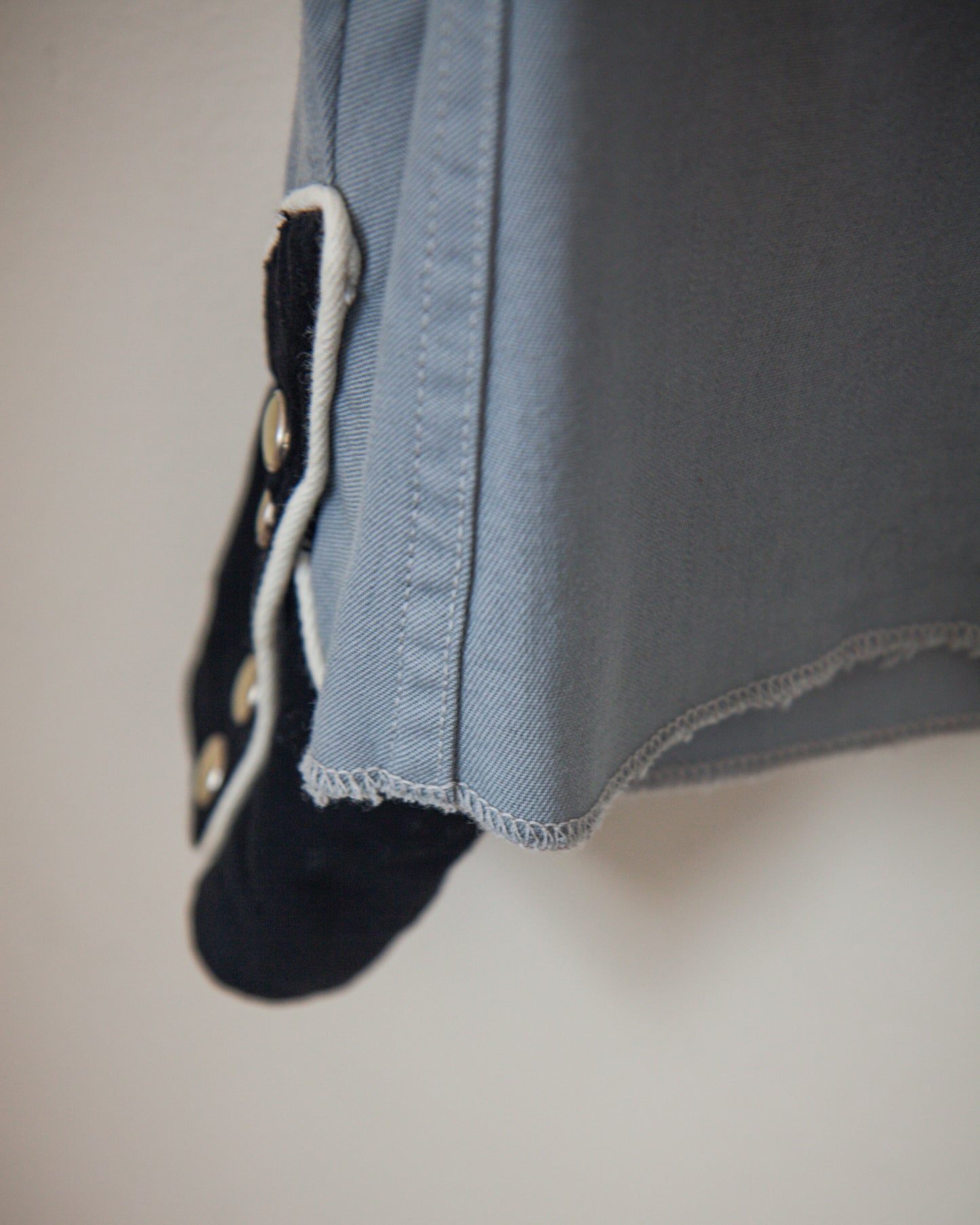 Close-up of a blue garment with button details on a neutral background