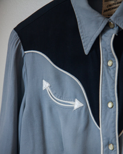 Close-up of a blue shirt with black accents and white arrow design on a plain background