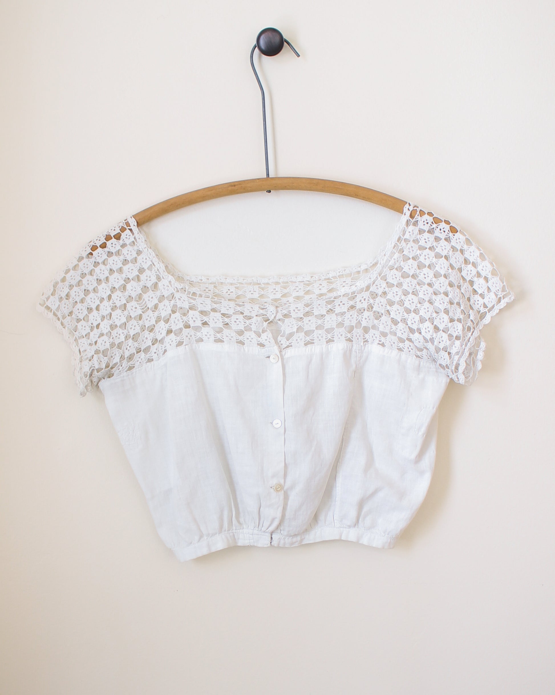 White lace crop top on a wooden hanger against a beige background