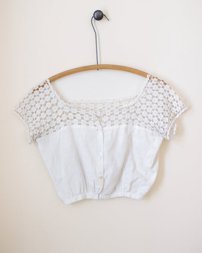 White lace crop top on a wooden hanger against a beige background