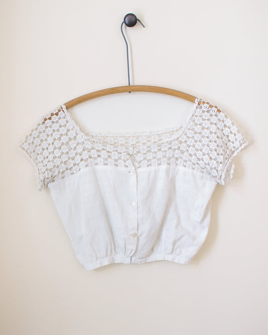 White lace crop top on a wooden hanger against a beige background