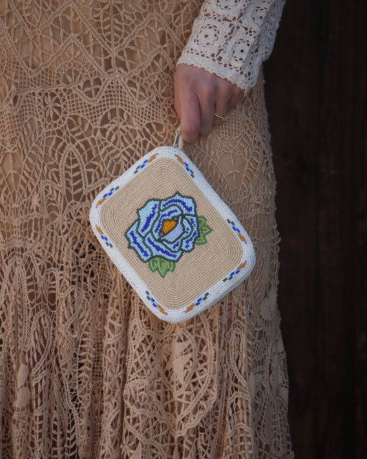 Handmade beaded purse with floral design held by a person wearing a lace dress.