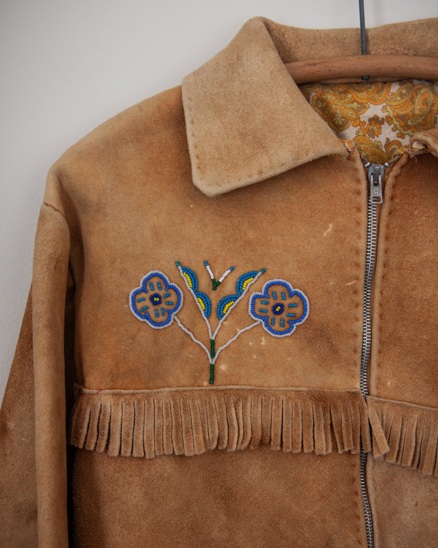 Brown suede jacket with floral embroidery and fringes on a plain background