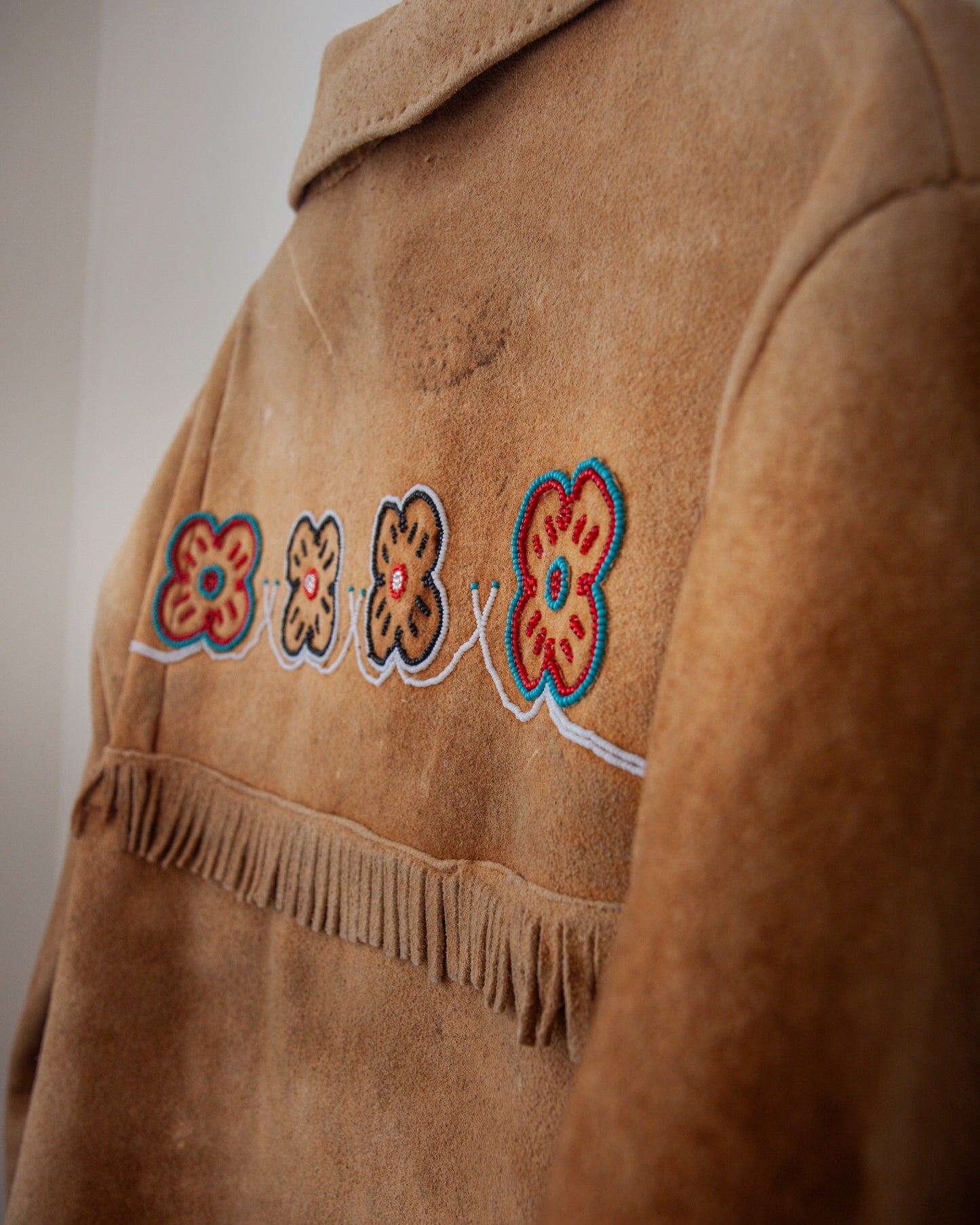 Brown suede jacket with floral embroidery and fringe details on a plain background