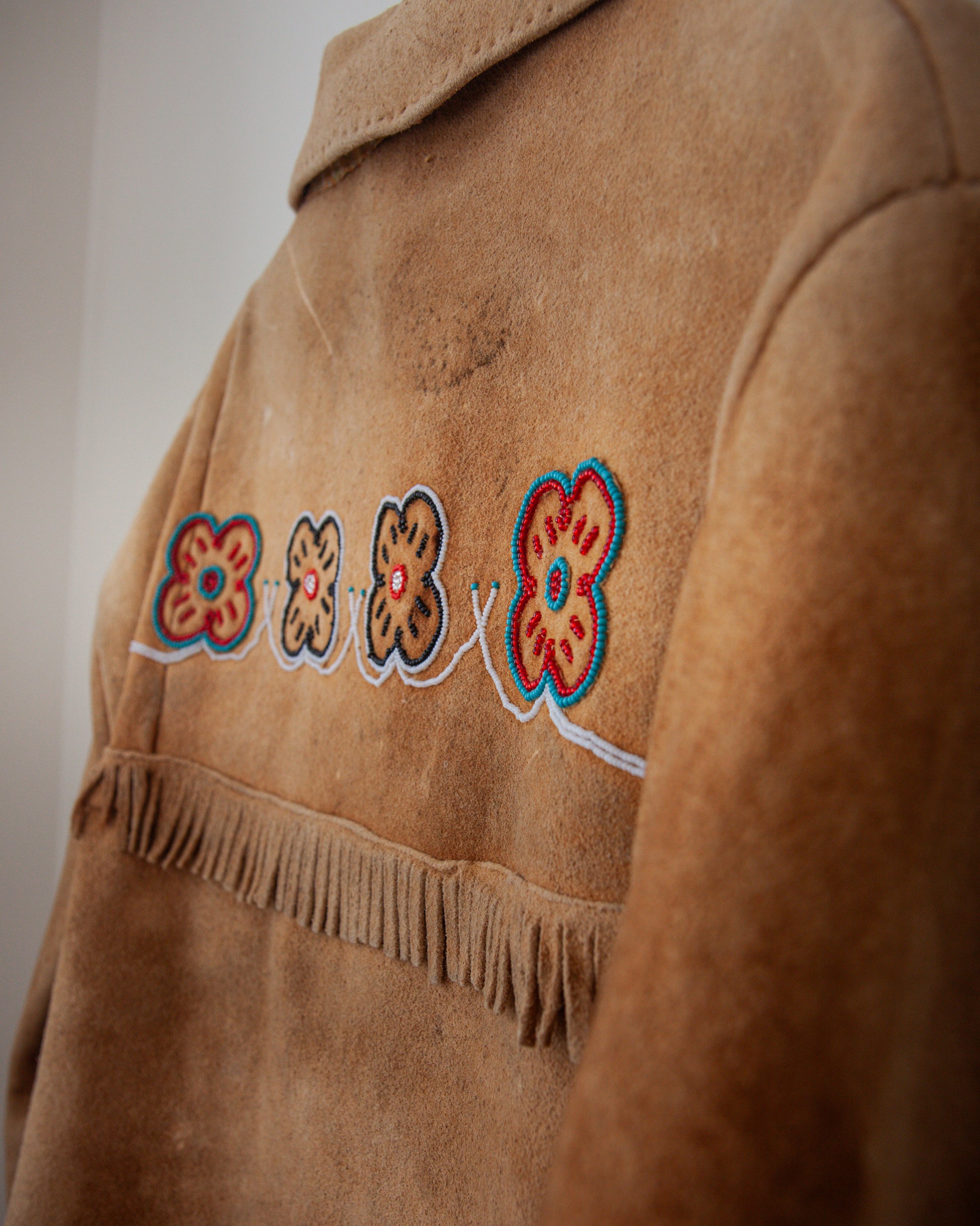 Brown suede jacket with floral embroidery and fringe details on a plain background