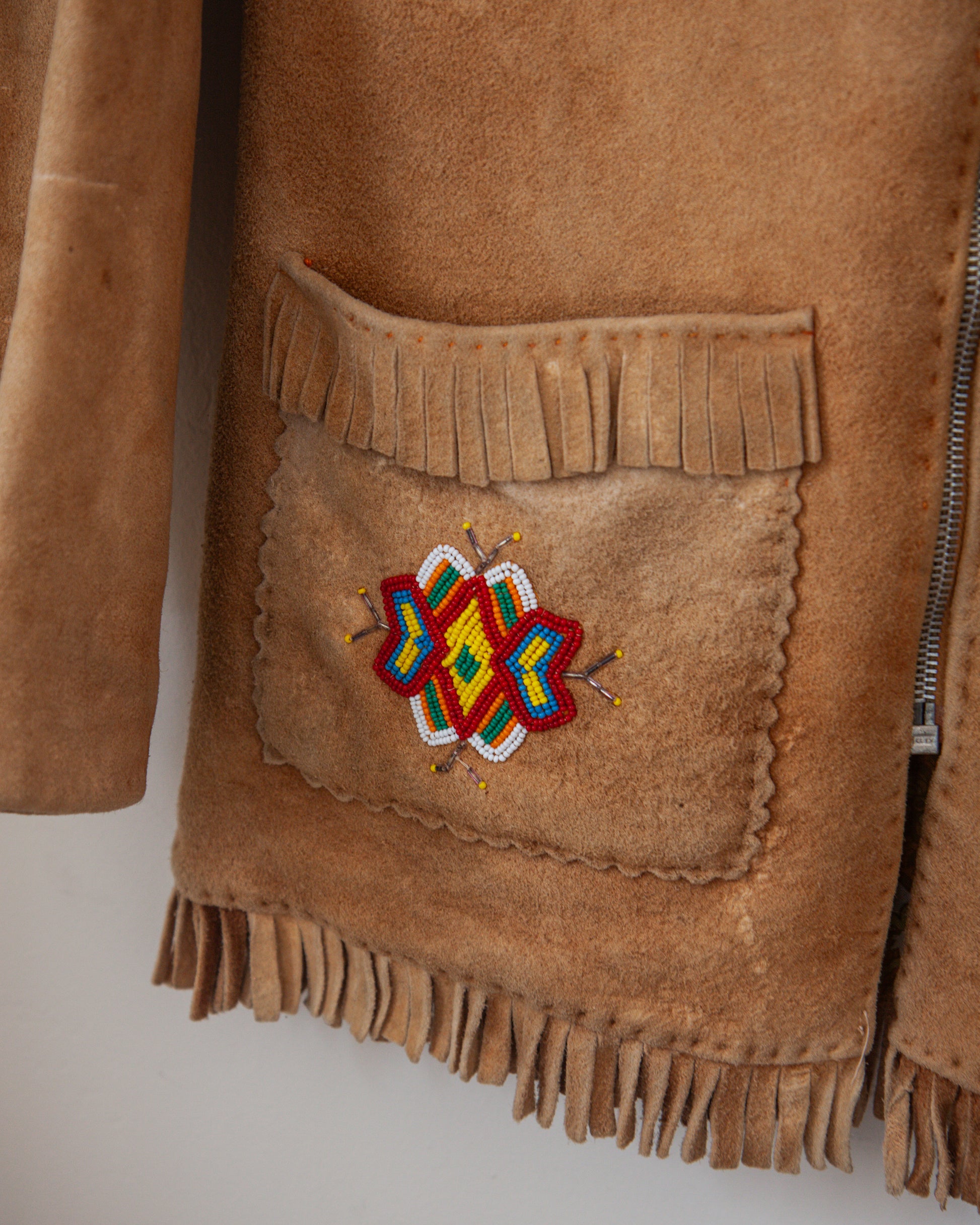 Brown suede jacket with a colorful embroidered patch on a white background