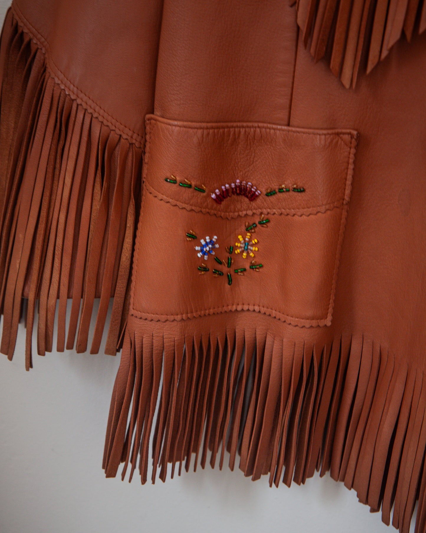 Brown leather jacket with fringe details and floral embroidery on a white background