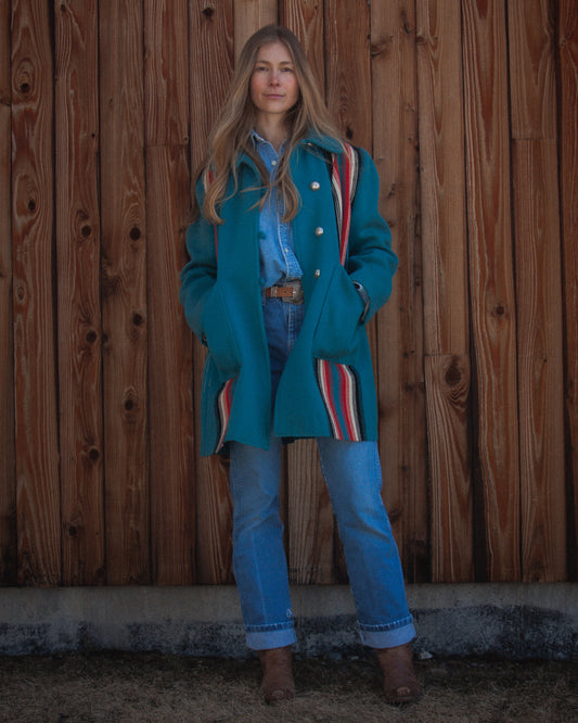Person wearing a blue coat with a striped pattern, standing against a wooden wall.