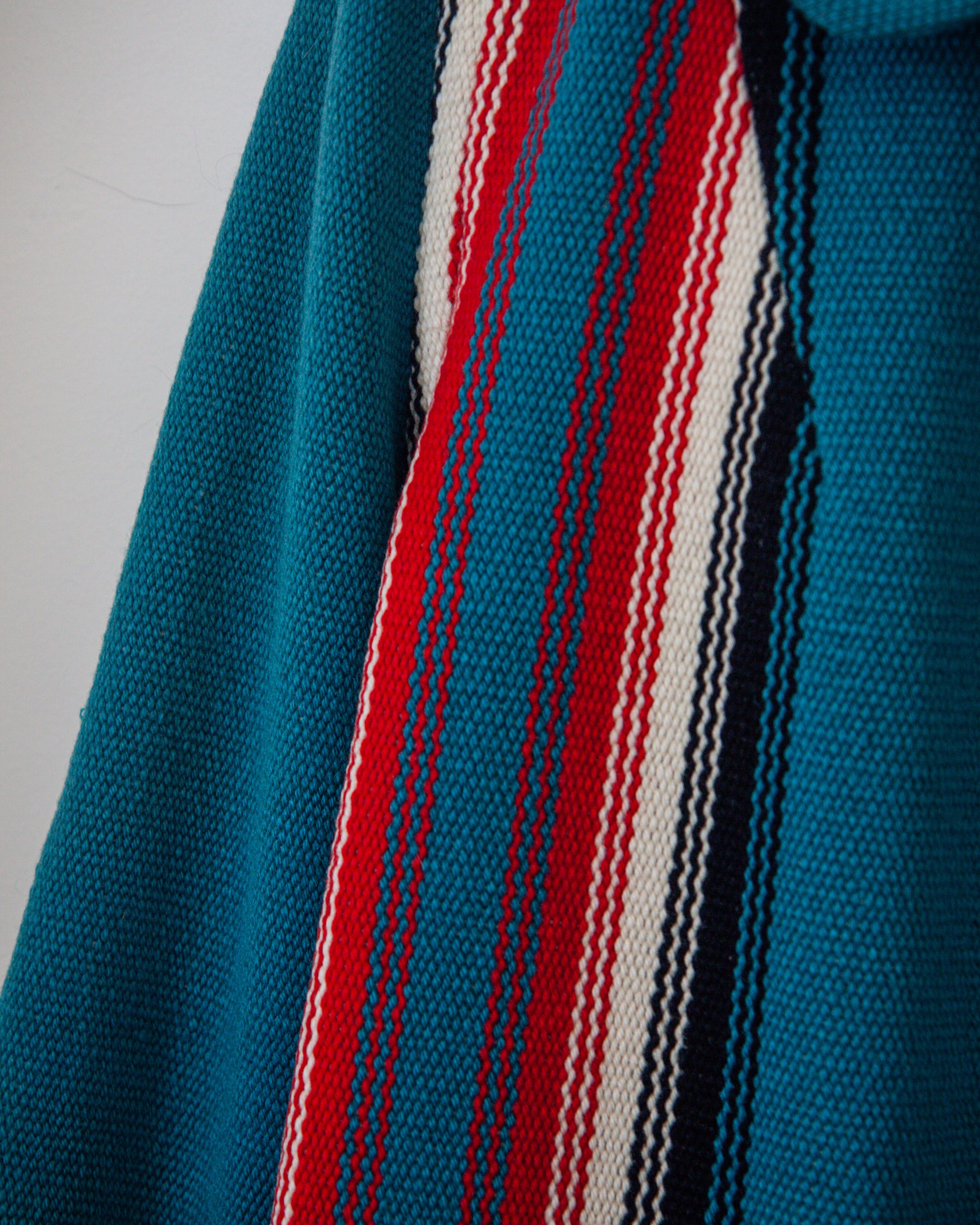 Close-up of a blue fabric with red, white, and black stripes on a plain background