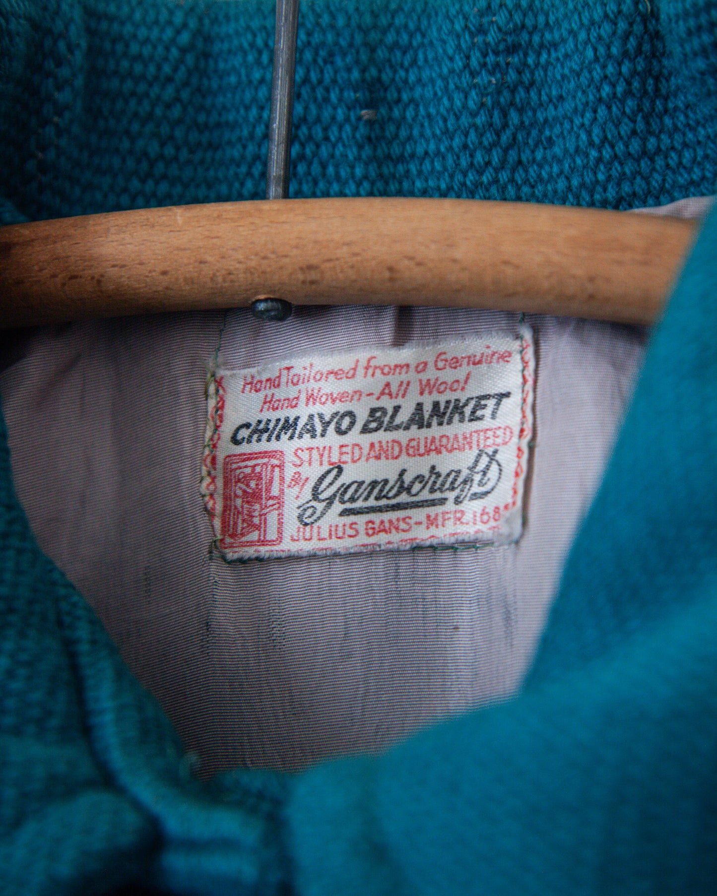 Close-up of a Ganscroft Chimayo Blanket label on a teal blanket with wooden handle.