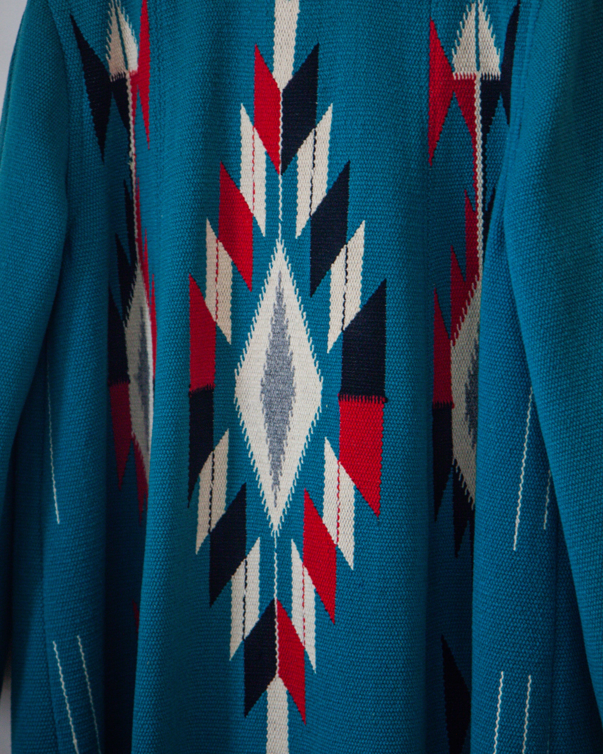 Close-up of a blue fabric with a geometric pattern featuring red, black, and white.