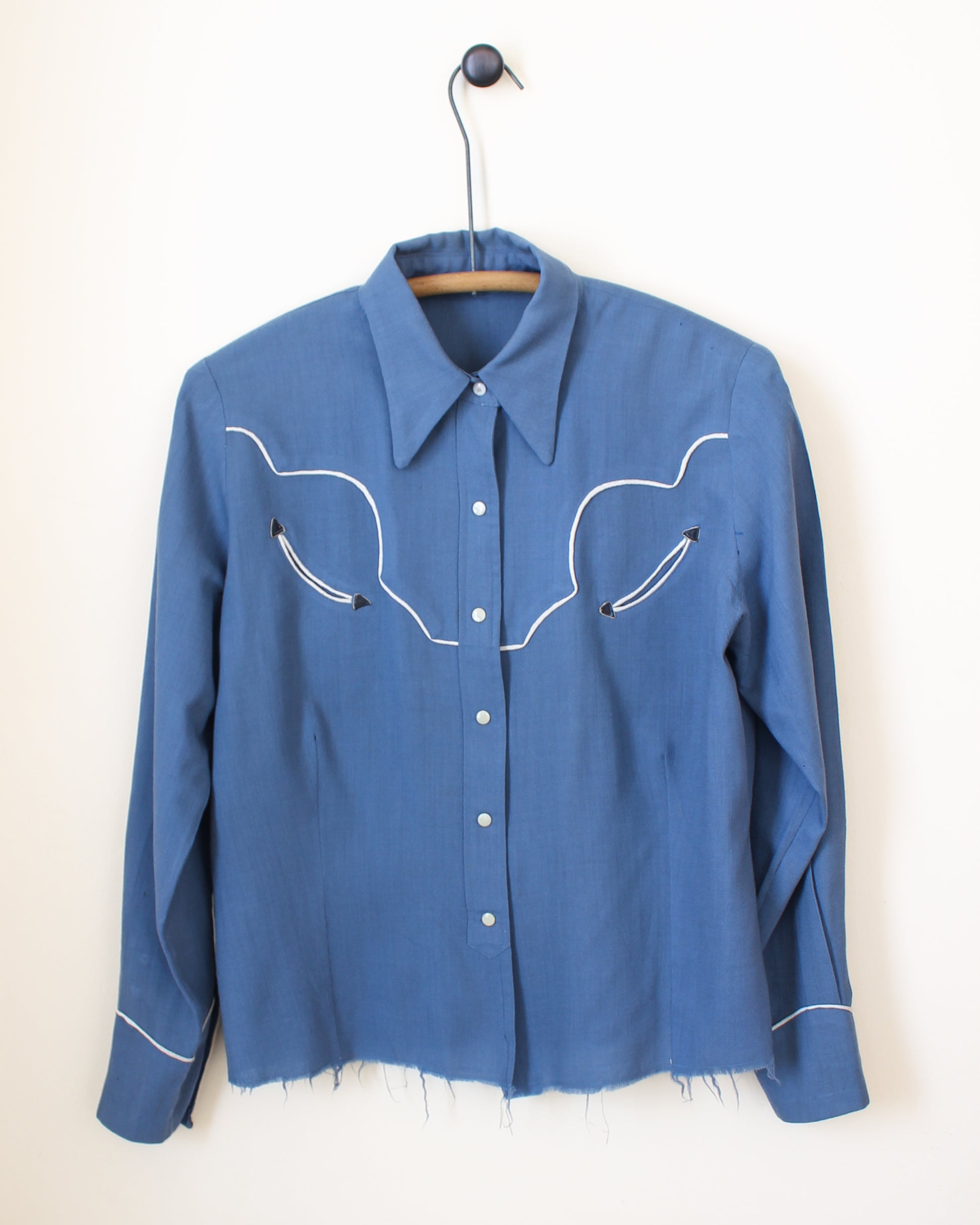 Blue shirt with white embroidery on a hanger against a white background