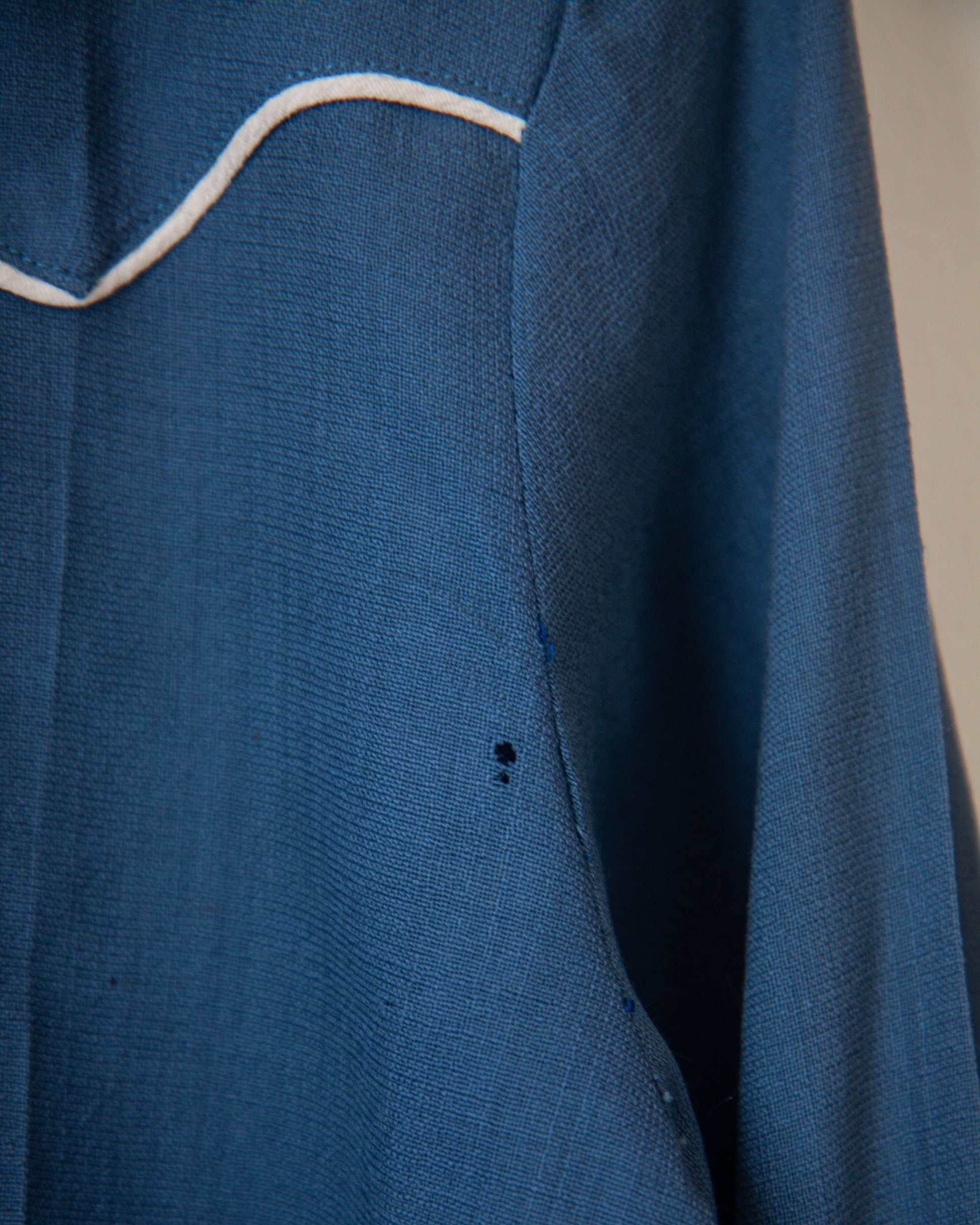Close-up of a blue garment with white stitching on a neutral background