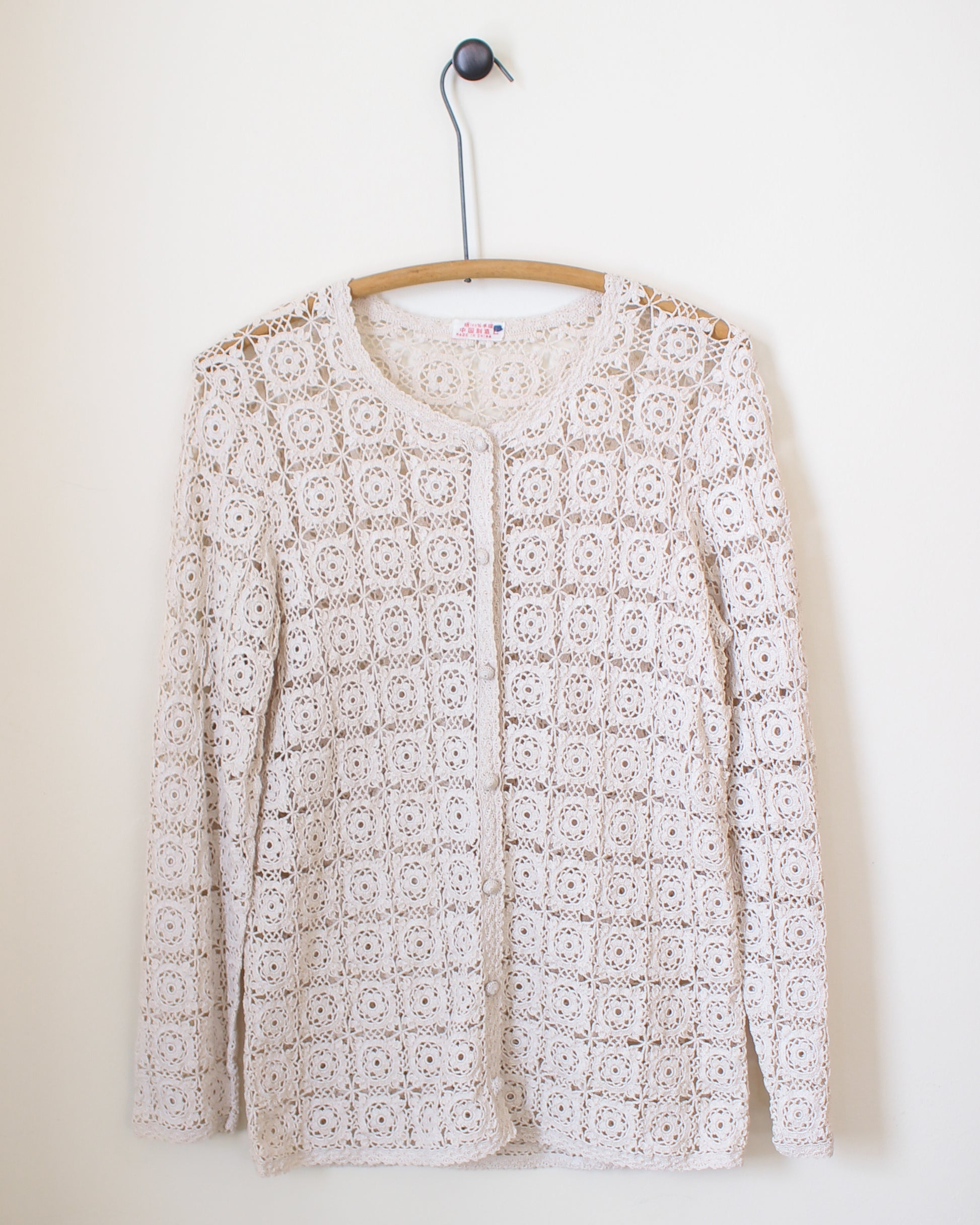 White lace cardigan on a hanger against a white background