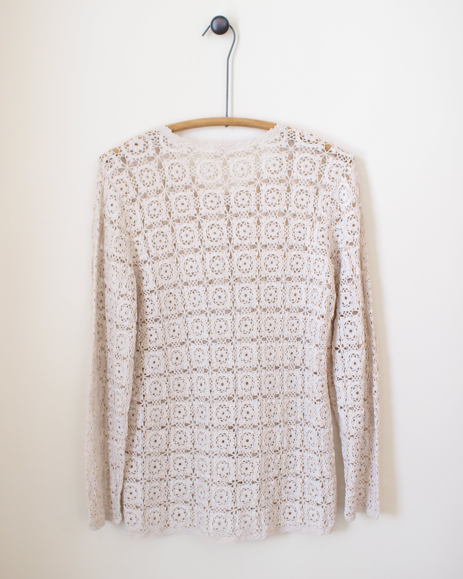 White crochet sweater on a wooden hanger against a white background