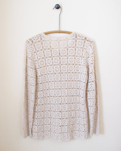White crochet sweater on a wooden hanger against a white background