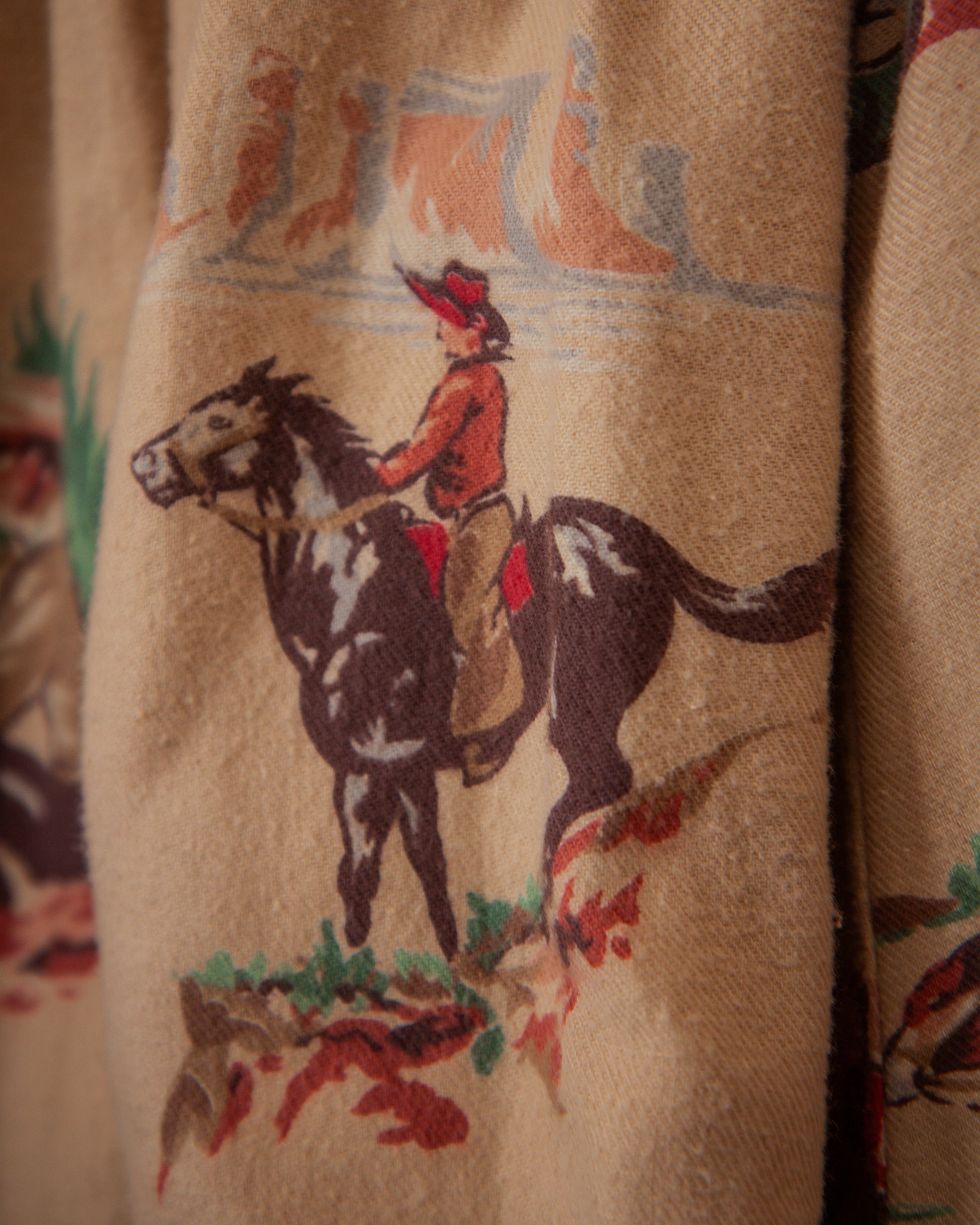 Close-up of a fabric with a cowboy riding a horse design on a beige background.