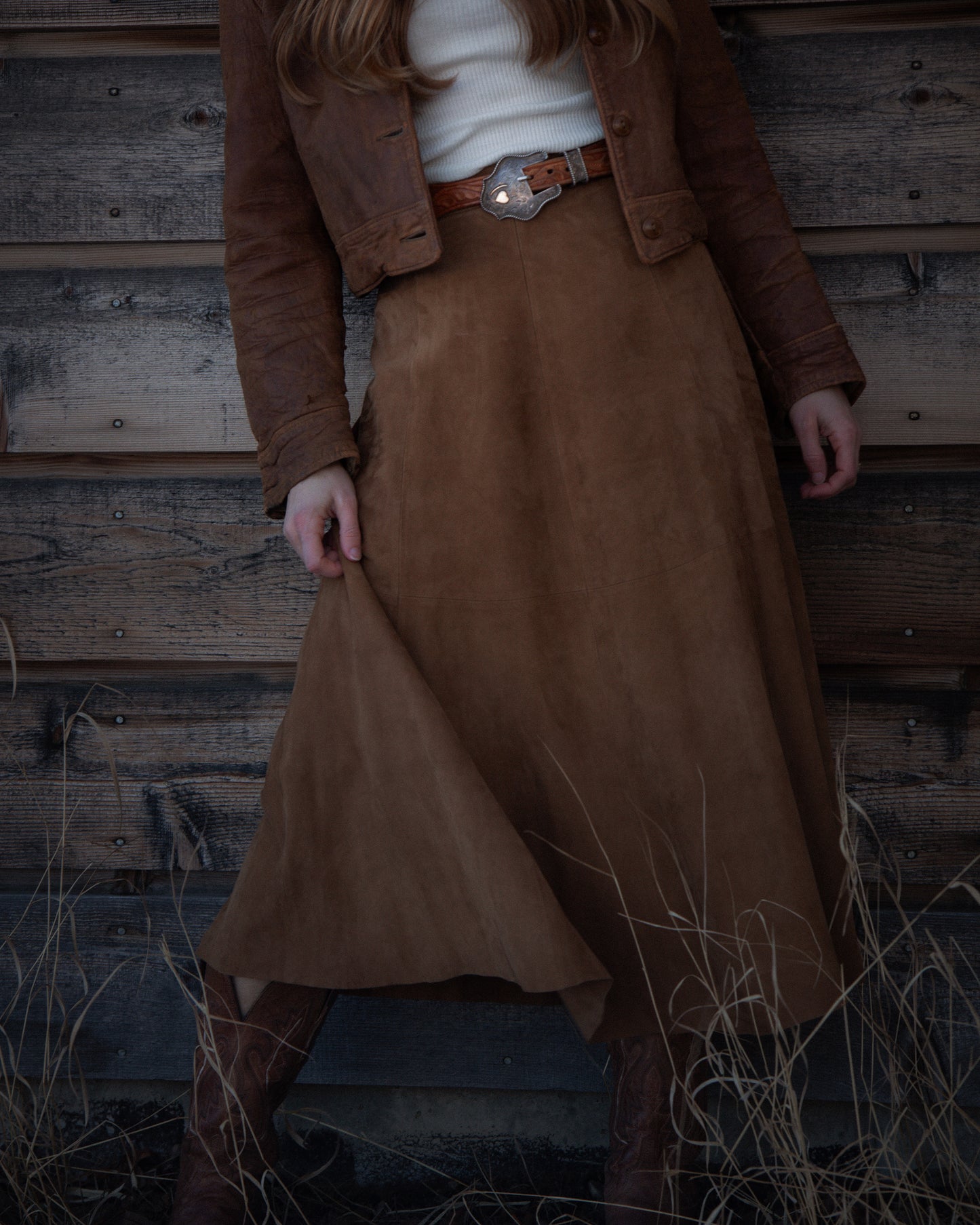 Person wearing a brown coat and skirt against a wooden wall.